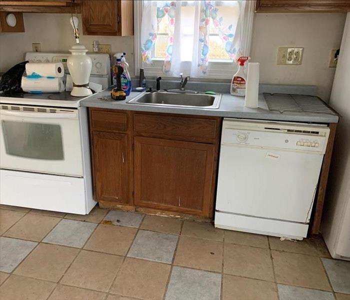 an old looking and dirty ktichen, brown counters, tan walls, tile floor, lamp, appliances