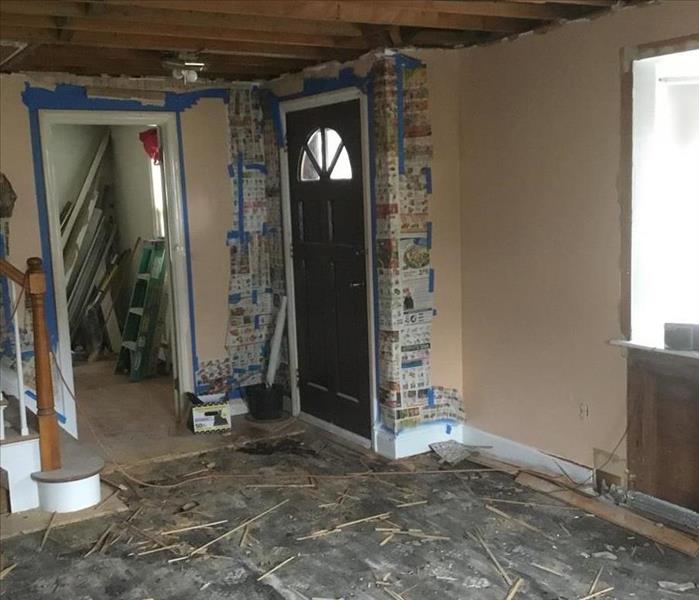 A living room with the floor mostly demoed, paper around the door way, tape, and obvious damage