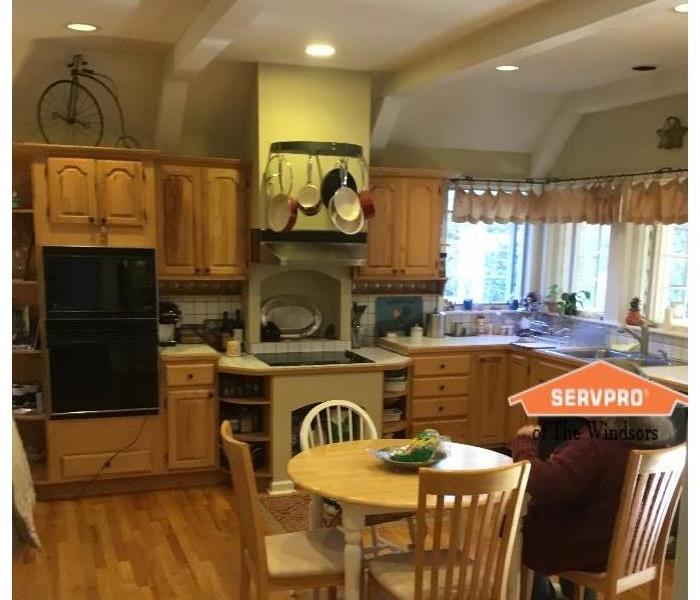 pciture of a kitchen with cabinets, white backsplash, table and four chairs, ceiling, recess lights, servpro logo