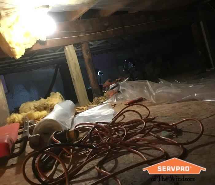Crawl Space with plastic containment barrier protecting insulation, twisted up orange cord on the floor & emergency light 