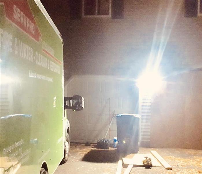 SERVPRO green van in a driveway one garage door boarded up, debris on the ground. 