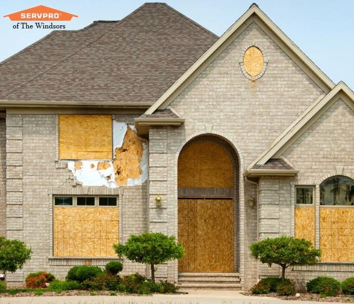 house with doors and windows boarded up, landscape, servpro logo, script that reads, "emergency board-up...
