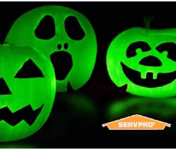 black background with three neon green pumpkins with carved out faces, servpro logo-orange with white script